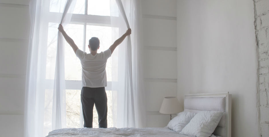 Home obrint les cortines per aprofitar la llum natural i estalviar energia a casa