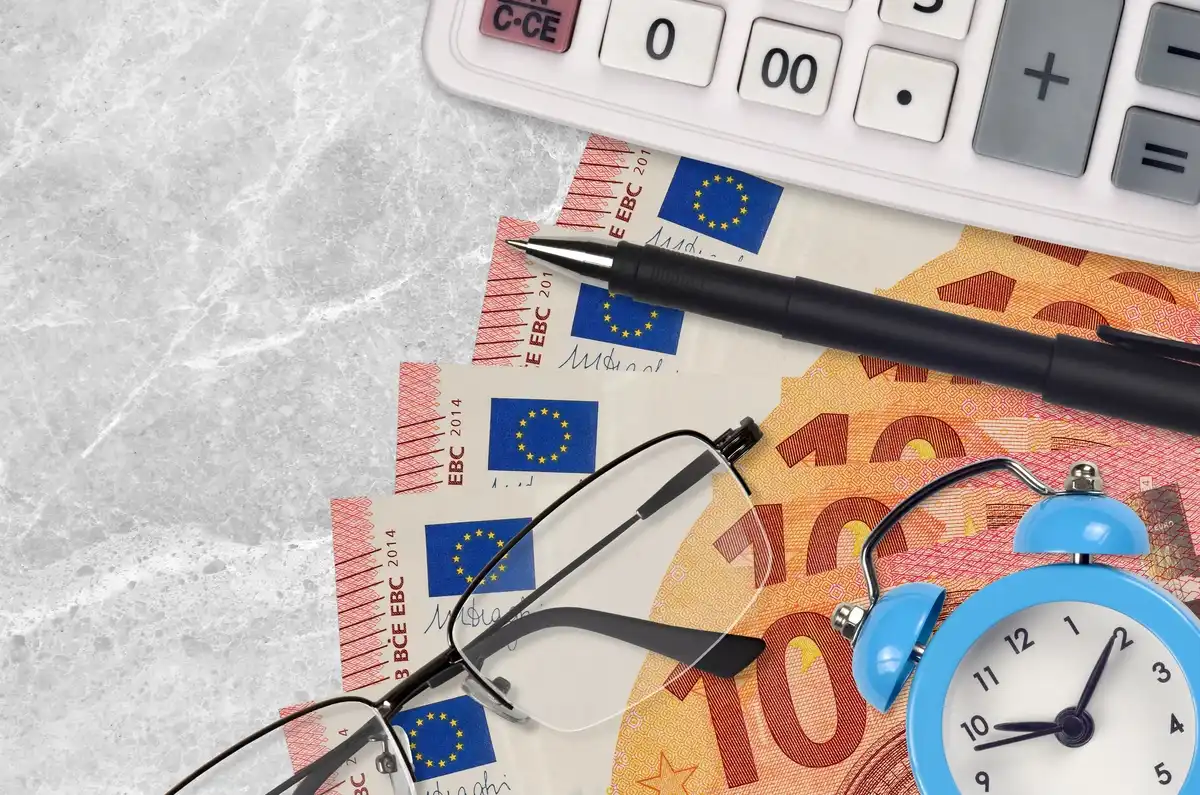 Billetes de 100 euros, calculadora y reloj, simbolizando ahorro programado.
