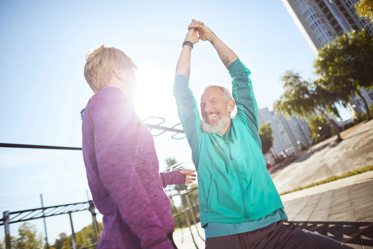 Pareja haciendo ejercicio sonriente al aire libre, promoviendo envejecimiento saludable activo.