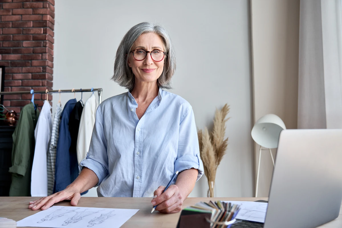 Cambiar de rumbo a los 55 o emprender a los 65: ¿por qué ha cambiado nuestro proyecto de vida? 3 Mujer sonriendo en su oficina, reinventando su carrera a los 55 años.