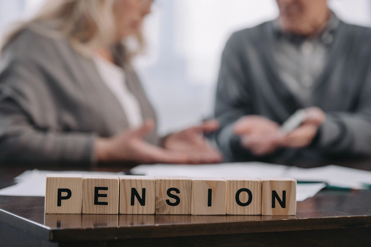 Bloques de madera con la palabra pensión y pareja mayor de fondo disfrutando tipos de pensiones.