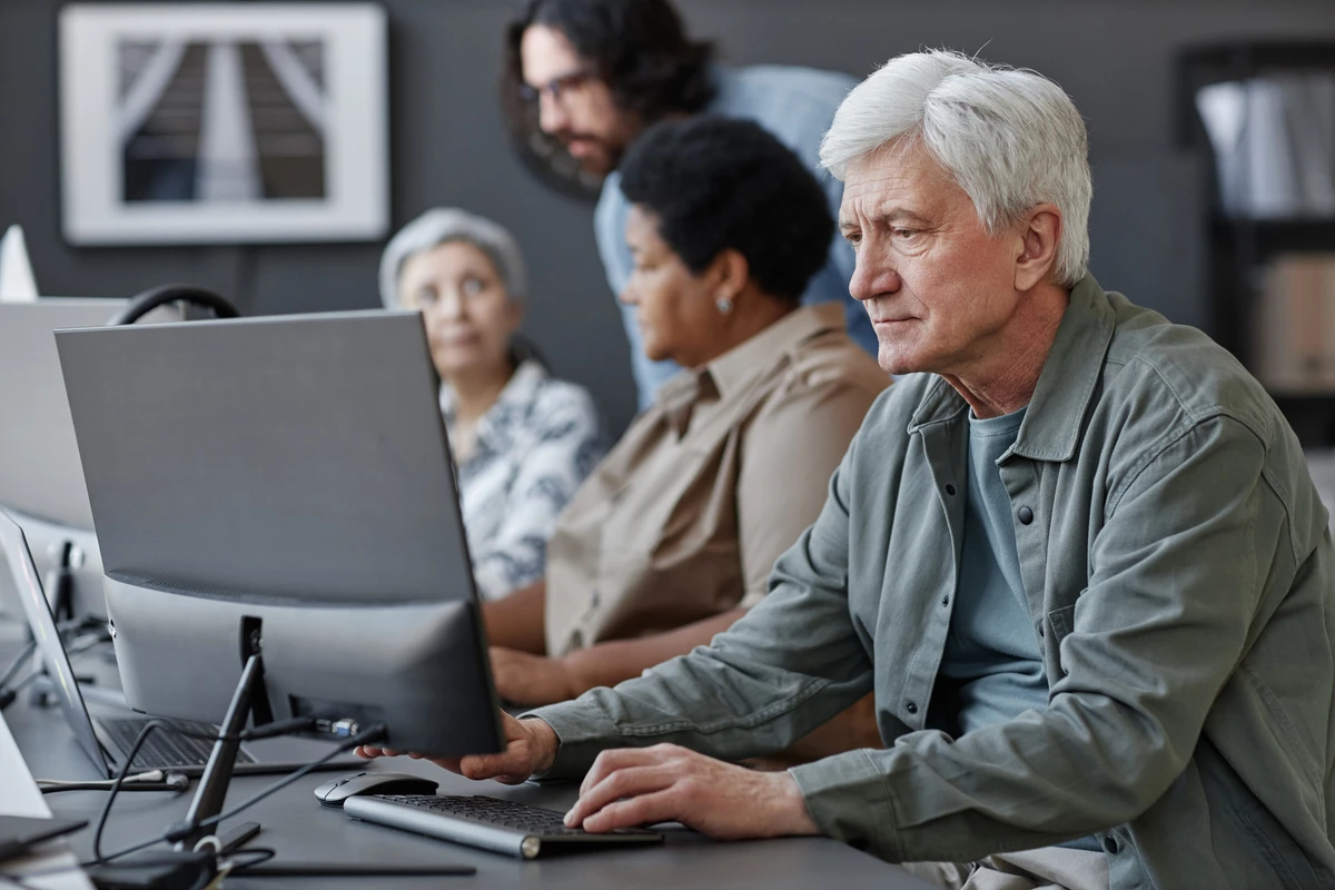 Un home gran treballant en ordinador en un curs de digitalització per a gent gran.