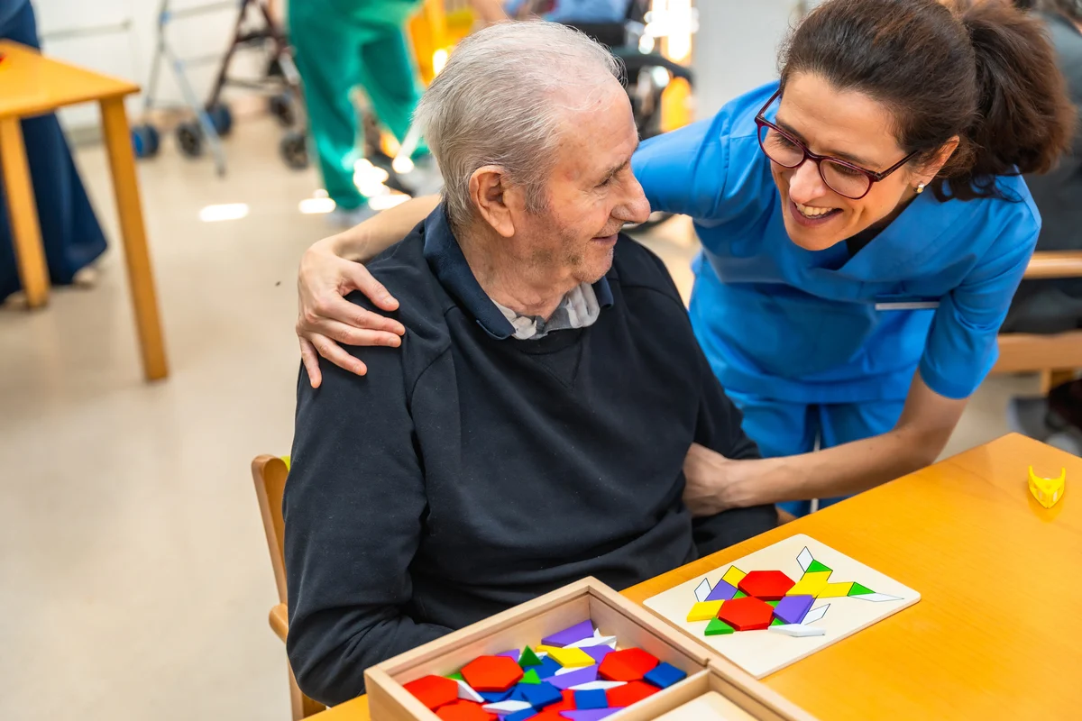 Home major amb símptomes alzheimer en teràpia cognitiva acompanyat cuidadora.