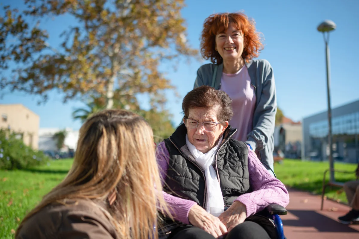 Dona gran amb Alzheimer acompanyada per cuidadores en un parc.